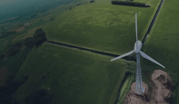 An aerial view of a large white wind turbine standing in green farmland fields