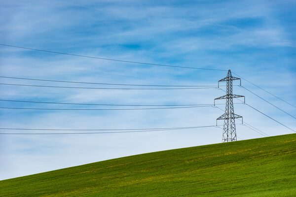 An electricity pylon with power lines crossing a green hillside under a blue sky