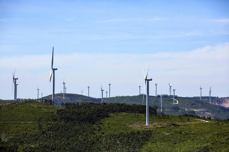 A wind farm with many white wind turbines spread across green hilly countryside under a blue sky