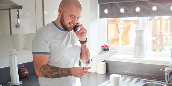 A man on the phone reading a paper bill in a UK kitchen