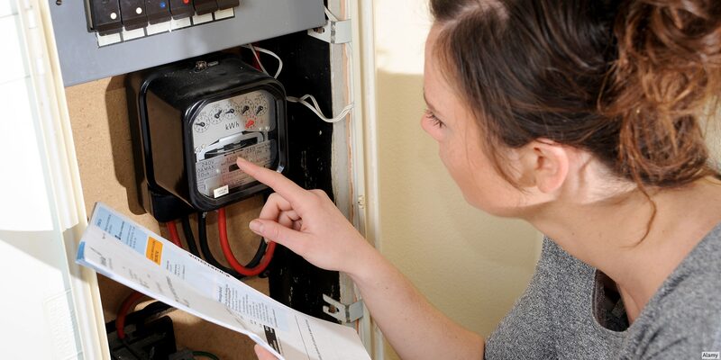 A woman pointing at an old analogue electricity meter in a cupboard while holding a bill