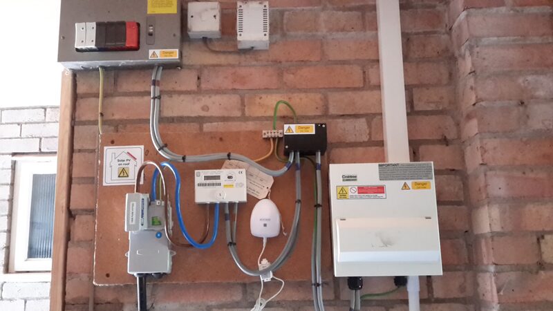 A consumer unit, electricity meter, isolator and white distribution box mounted on a brick wall with exposed wiring