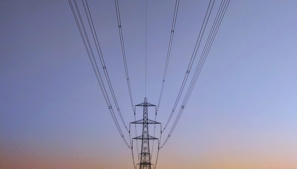 A row of electricity transmission pylons with power lines silhouetted against a dusk sky