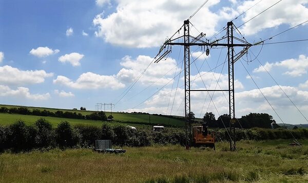 Electricity transmission pylons and power lines in a grassy Dorset field with maintenance equipment nearby