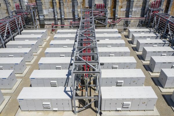 A large grid-scale battery energy storage installation with rows of white battery containers and steel cable racks