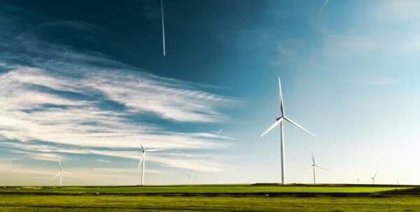Wind turbines standing in a green field under a blue sky with clouds