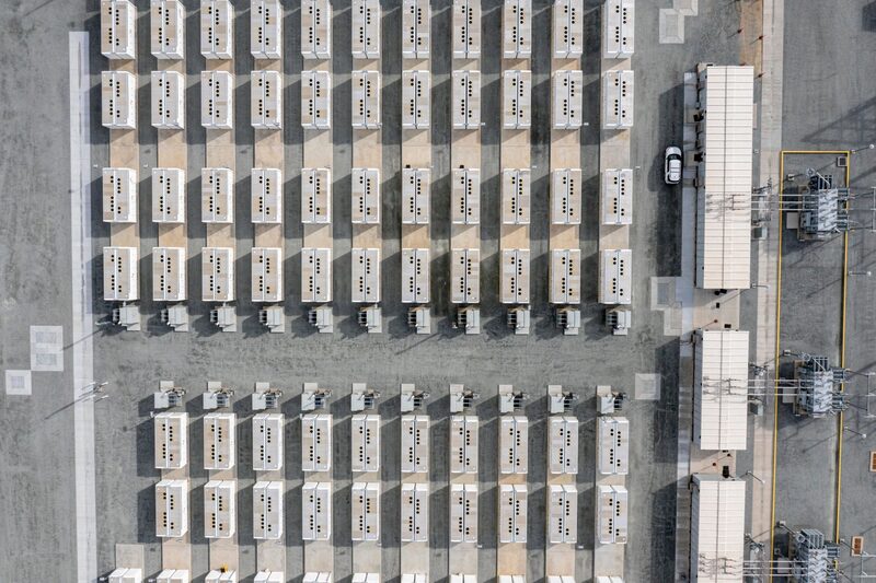 Aerial view of a large grid-scale battery energy storage site with rows of white battery containers and electrical equipment