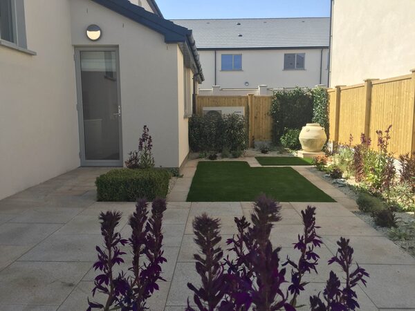 A small modern garden with an air source heat pump unit mounted on the exterior wall of a house