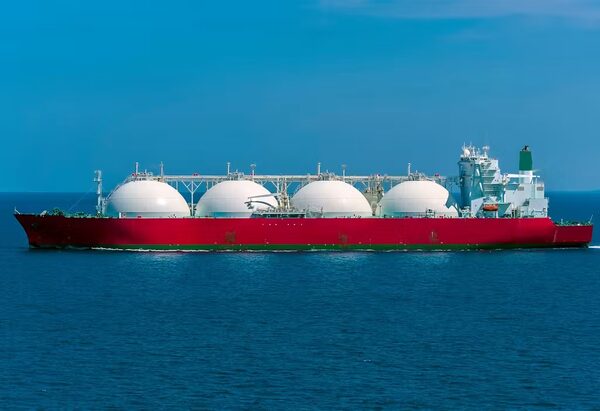 A red LNG tanker ship with four white spherical gas tanks sailing on the ocean under a blue sky
