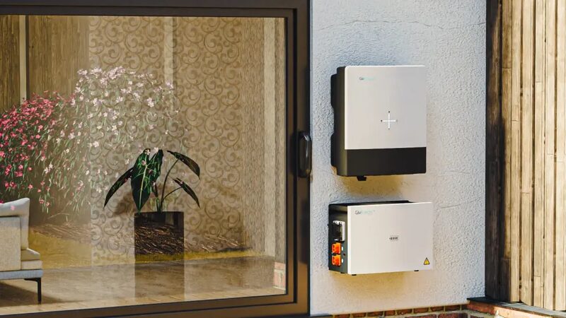 A GivEnergy home battery and inverter mounted on an exterior wall next to a window