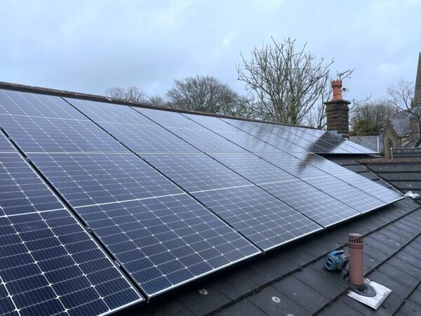 Solar panels installed on a slate-tiled house roof with a chimney and bare trees behind