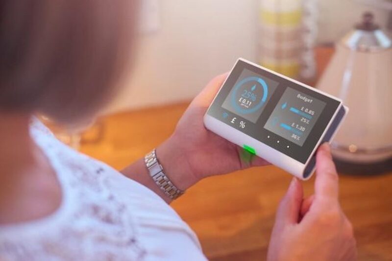 A woman holding a smart meter in-home display showing energy usage and budget figures