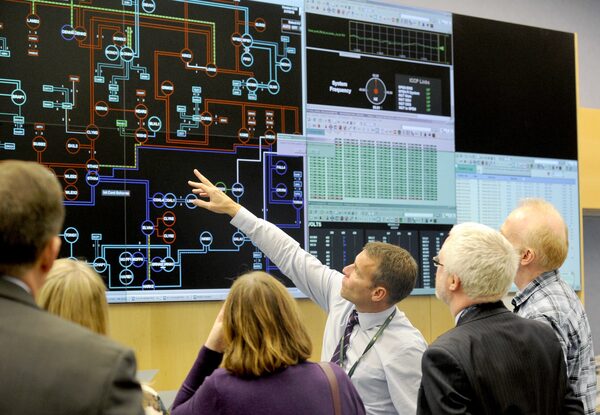 People in an electricity network control room looking at large screens displaying grid schematics and system data