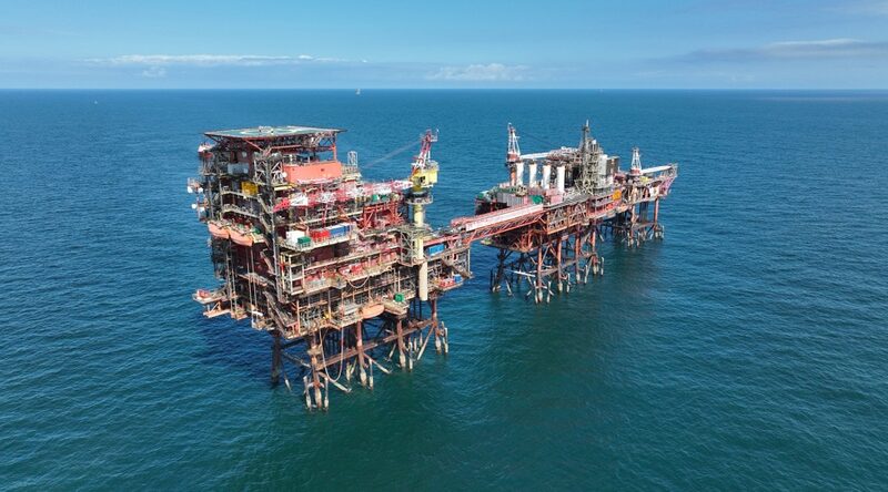 An aerial view of a large offshore gas platform standing in calm blue sea under a clear sky