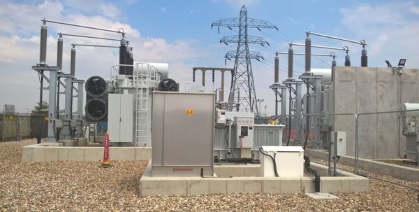 An outdoor electricity substation with transformers, switchgear and a pylon under a blue sky