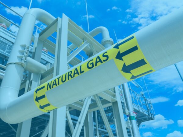 An industrial natural gas pipeline with a yellow 'NATURAL GAS' label and directional arrows against a blue sky
