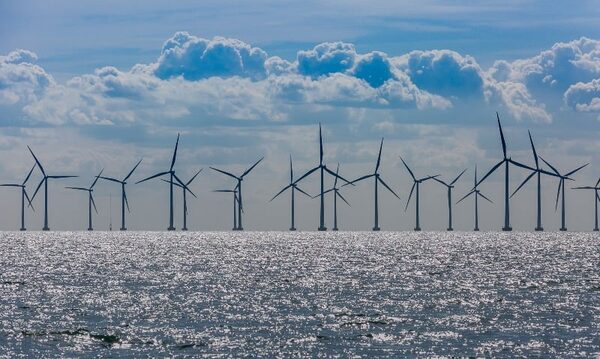 An offshore wind farm with many wind turbines standing in the sea under a cloudy sky