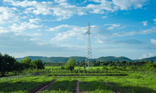 An electricity transmission pylon standing in a green rural landscape under a blue cloudy sky