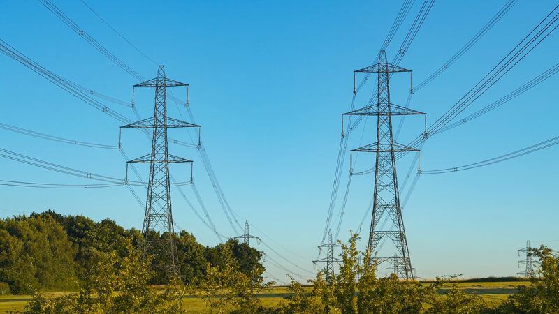 High-voltage electricity pylons and transmission lines crossing green countryside under a clear blue sky