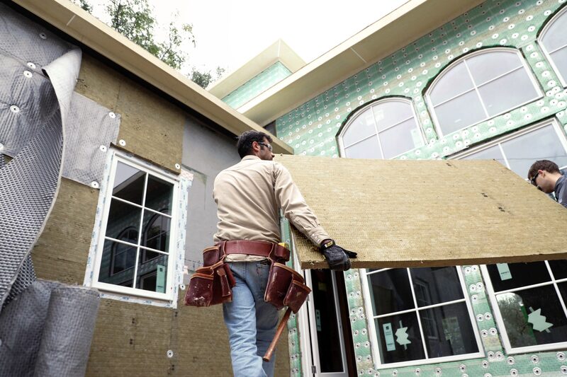 Workers carrying a large Rockwool insulation board while installing external wall insulation on a house under construction