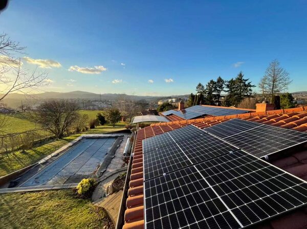 Solar panels installed on a terracotta-tiled house roof overlooking a garden with a covered swimming pool and countryside hills