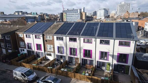 A row of retrofitted terraced houses with large rooftop solar panel arrays and colourful window surrounds in a UK city street