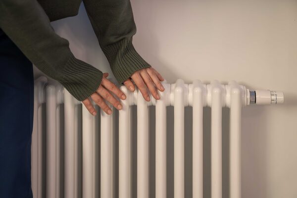A person warming their hands on a white column radiator mounted on a wall
