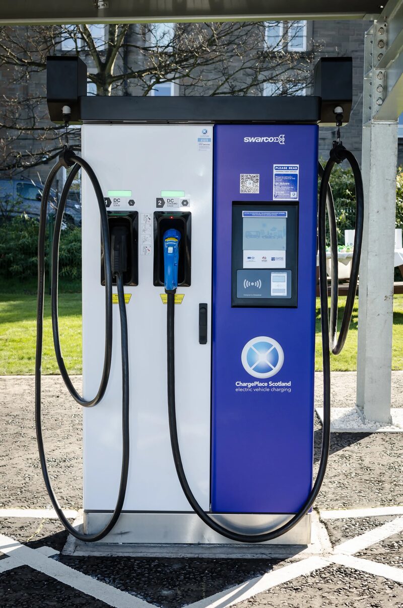 A Swarco ChargePlace Scotland public electric vehicle charging point with two tethered cables under a canopy