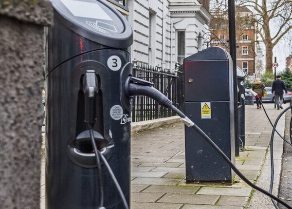 A black on-street EV charge point with a cable plugged in on a UK pavement