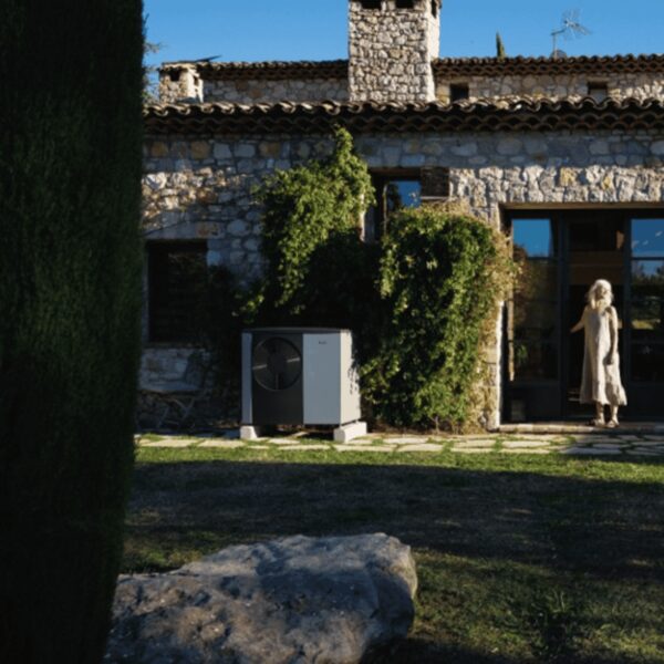 An outdoor air source heat pump unit installed on the lawn outside a stone country house with a woman standing at the door