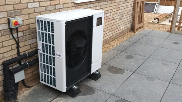 An air source heat pump unit installed outside a brick house on a paved patio