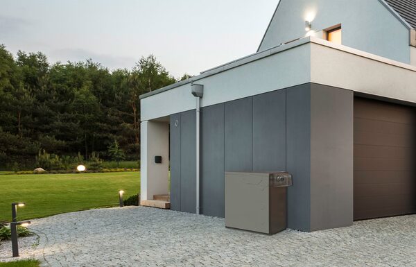 A grey outdoor oil boiler cabinet installed against the wall of a modern house beside the garage