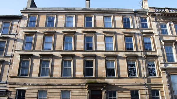 The stone facade of a historic Scottish tenement building with rows of sash windows on each storey