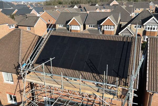 Aerial view of a UK house with scaffolding and black solar panels on its tiled roof, surrounded by similar houses