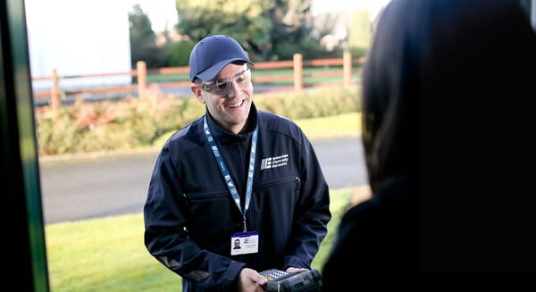 A Northern Ireland Electricity Networks meter reader in branded uniform and ID lanyard greeting a householder at the front door