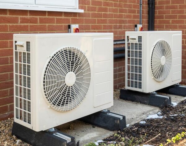 Two air source heat pump units installed outside a brick house wall