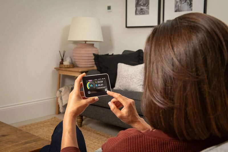 A woman using a smart energy display (in-home display) showing energy usage and cost in a living room