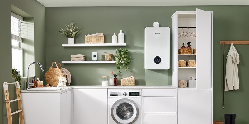A wall-mounted white combi gas boiler installed in a green utility room above a washing machine and white cabinetry