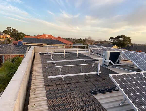 A flat residential roof with solar panel mounting rails, some installed solar panels and an air conditioning unit, overlooking suburban rooftops