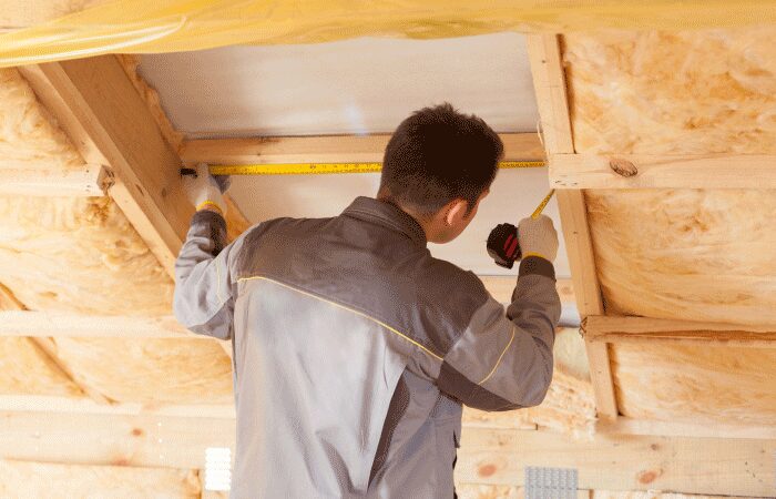A workman in a loft measuring between joists surrounded by mineral wool insulation