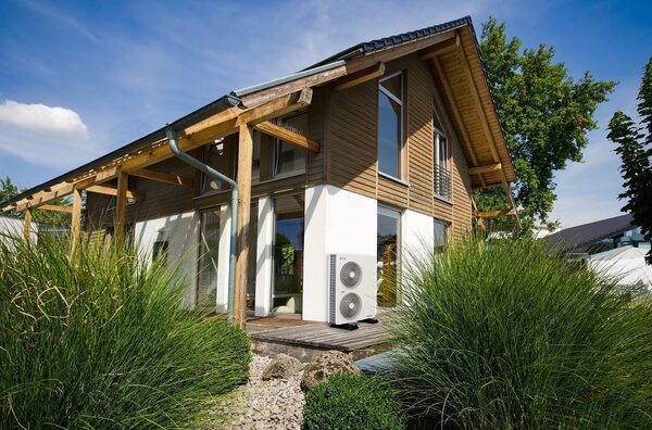 A modern timber-clad house with an air source heat pump unit installed on the exterior wall beside the deck