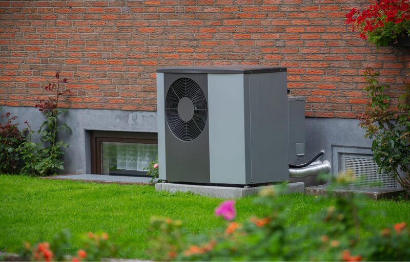An air source heat pump unit installed outside a red brick house on a concrete base beside a lawn