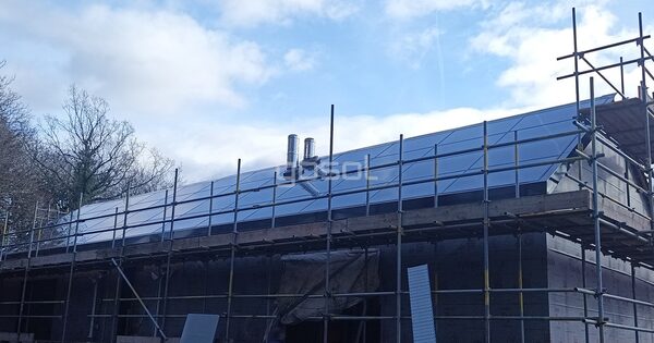 A house under construction surrounded by scaffolding with a full in-roof solar panel array on its roof