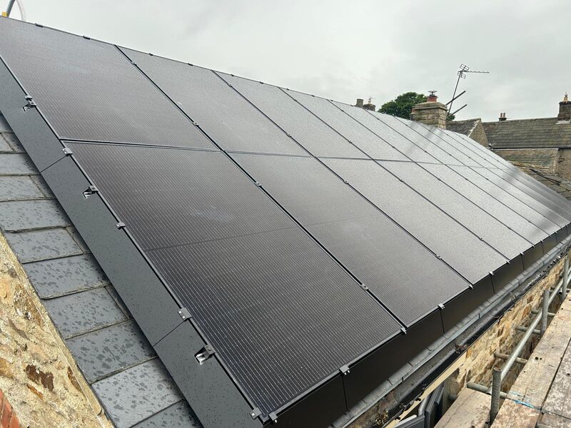 Black solar panels fitted flush on the slate roof of a stone house, with scaffolding alongside
