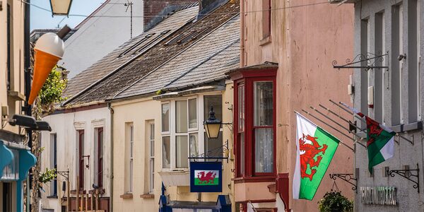 A street of terraced houses and shopfronts in a Welsh town with Welsh flags hanging from the buildings