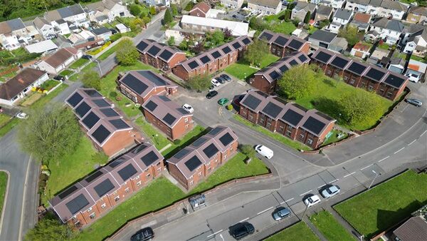Aerial view of a brick social housing estate in Wales with dark solar panels installed across many pitched roofs