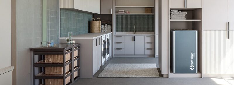A grey Ecoforest domestic hot water heat pump cylinder installed in a utility room with washing machine, sink and storage cabinets