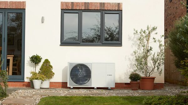 A Bosch air source heat pump installed on the exterior wall of a house beside a patio with potted plants