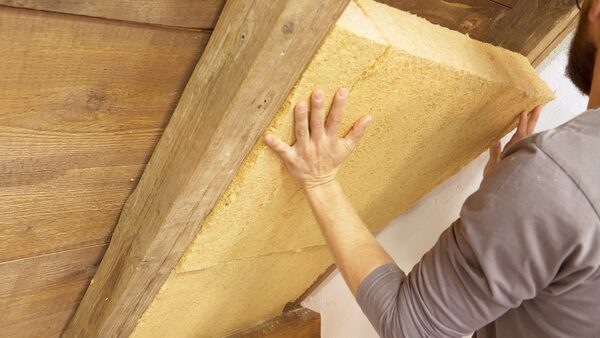 A man fitting a wood-fibre insulation board between wooden roof rafters