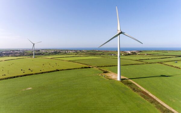 Wind turbines standing in green coastal farmland with fields, grazing cows and the sea in the distance
